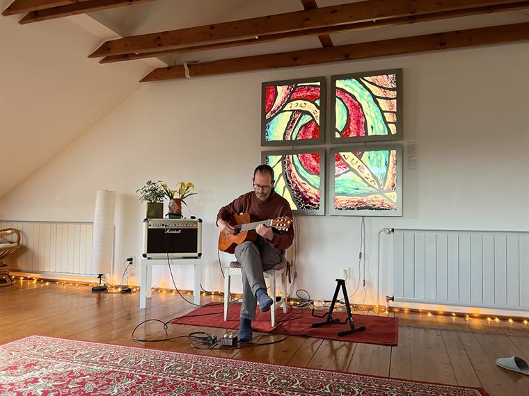 Gitározó ember a tetőtérben, háttérben üvegfestményekkel